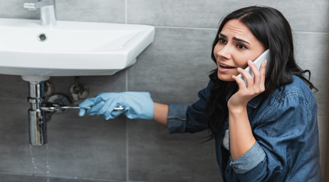 Stressed girl repairing pipe with wrench and talking on smartphone Stressed girl repairing pipe with wrench and talking on smartphone